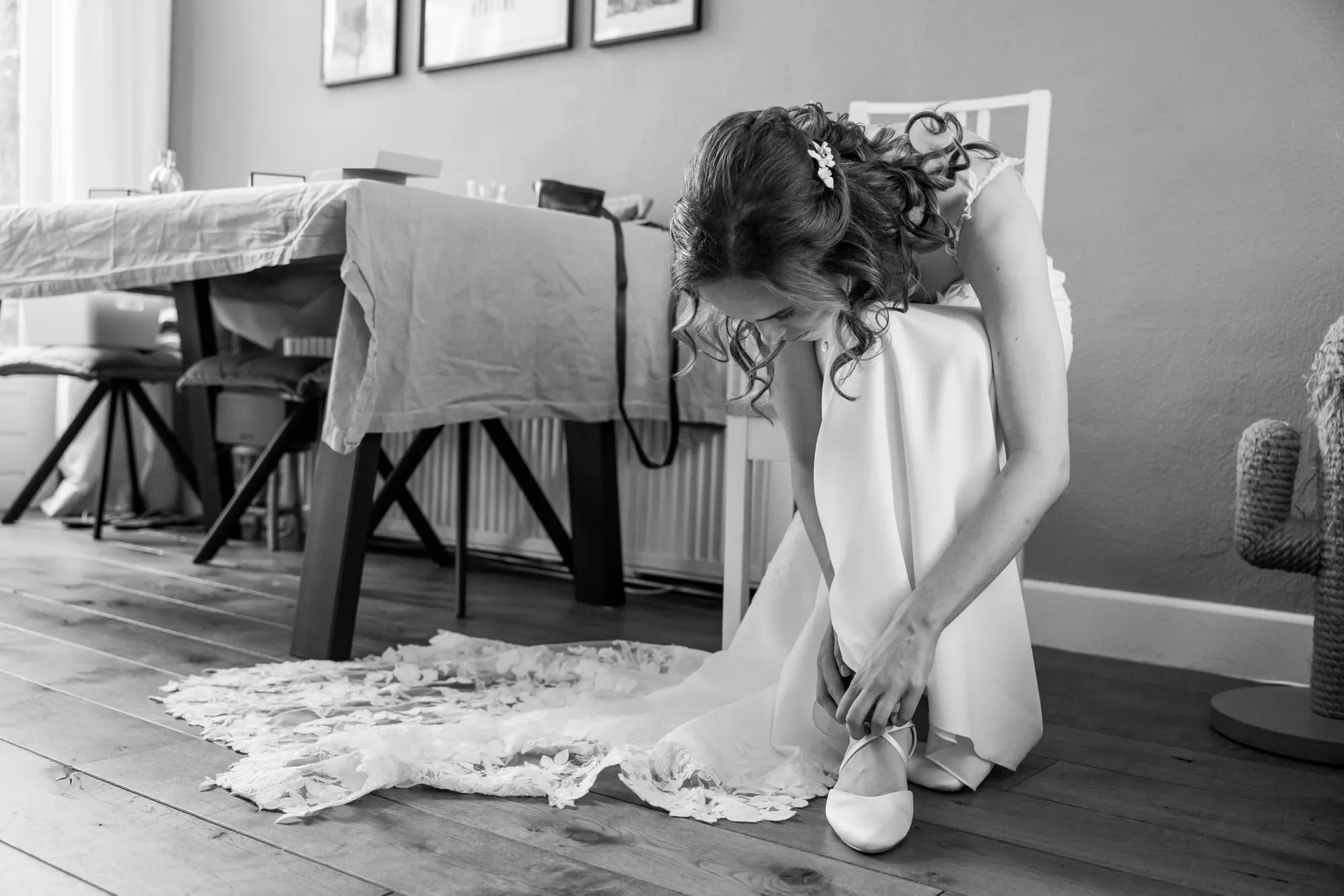 Zwart-witbeeld van de bruid die voorovergebogen haar schoenen aandoet