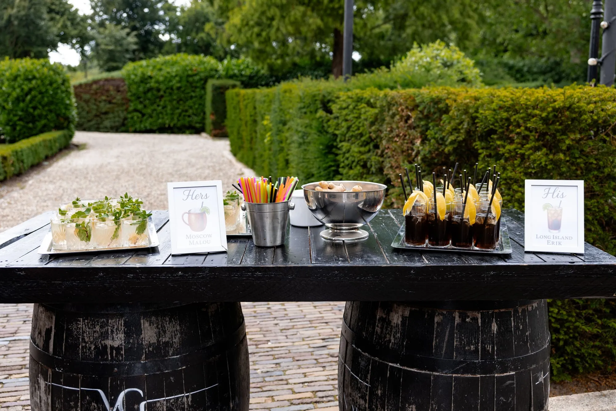 Borreltafel in de tuin op wijnvaten met glazen, hapjes en handgeschreven bordjes