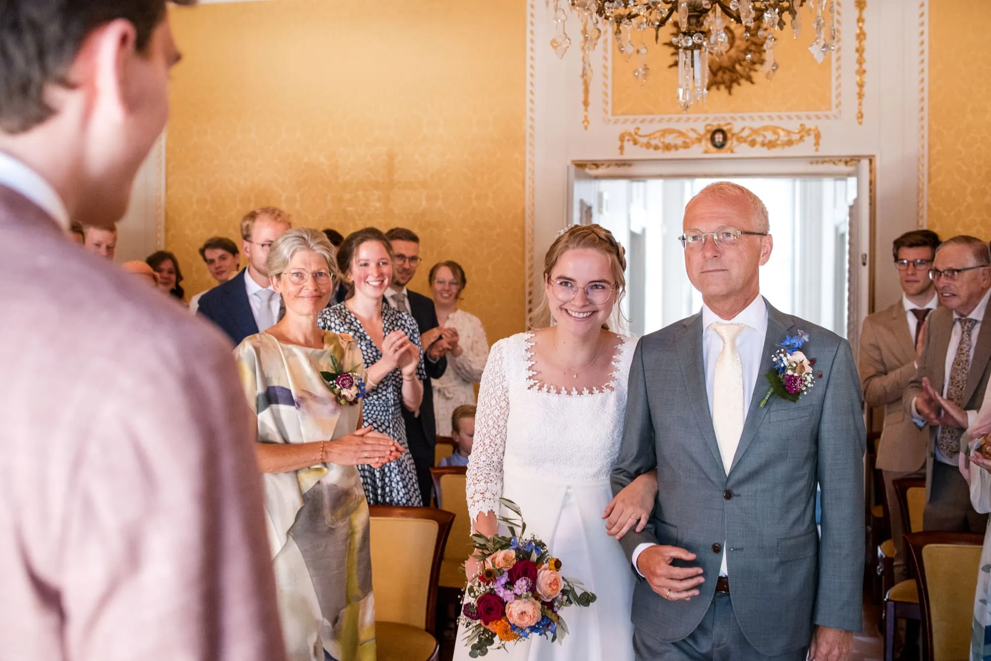 Bruid komt binnen aan de arm van haar vader, tussen de applaudisserende gasten