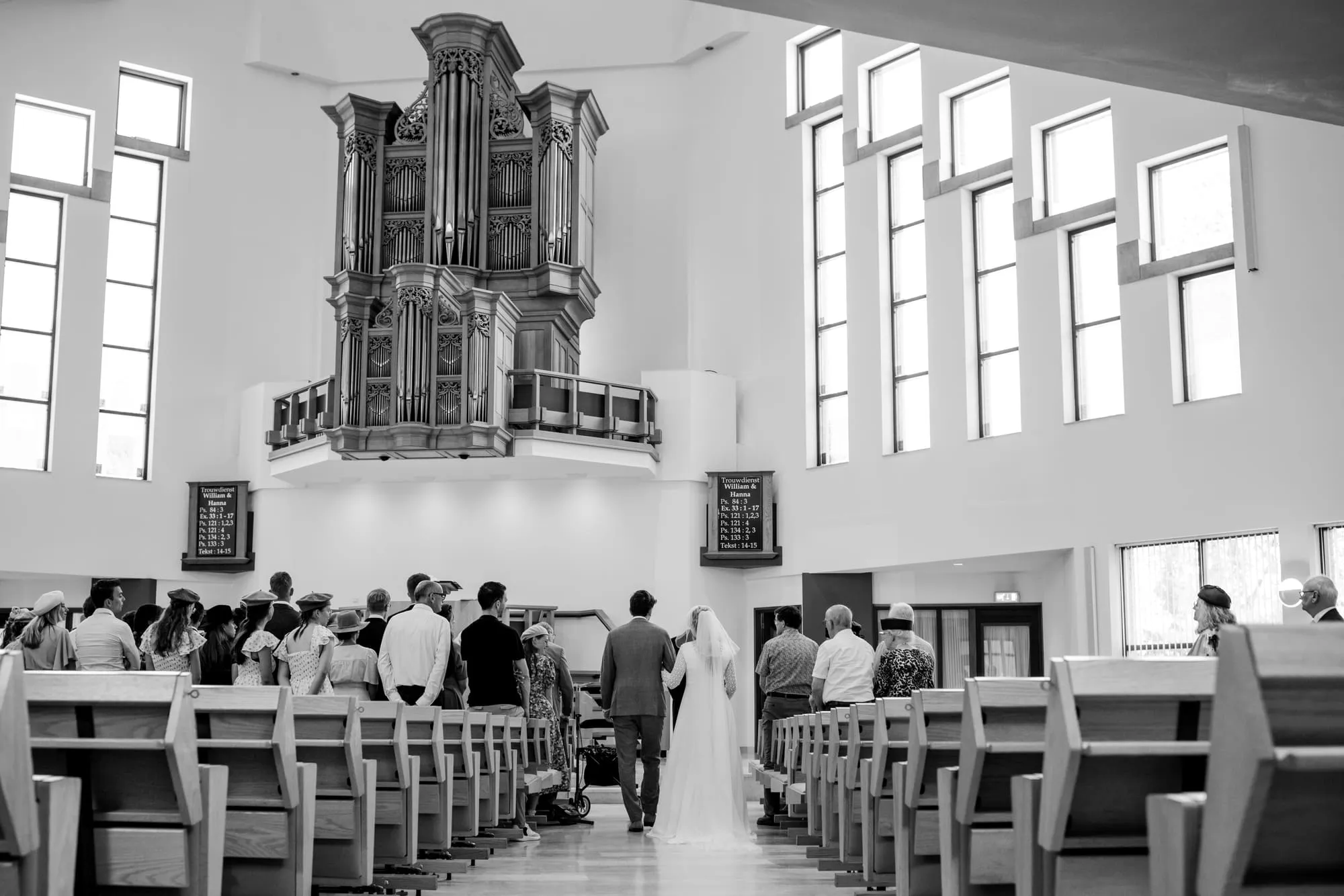 Zwart-witbeeld van het bruidspaar in het gangpad van de kerk, met het orgel op de achtergrond
