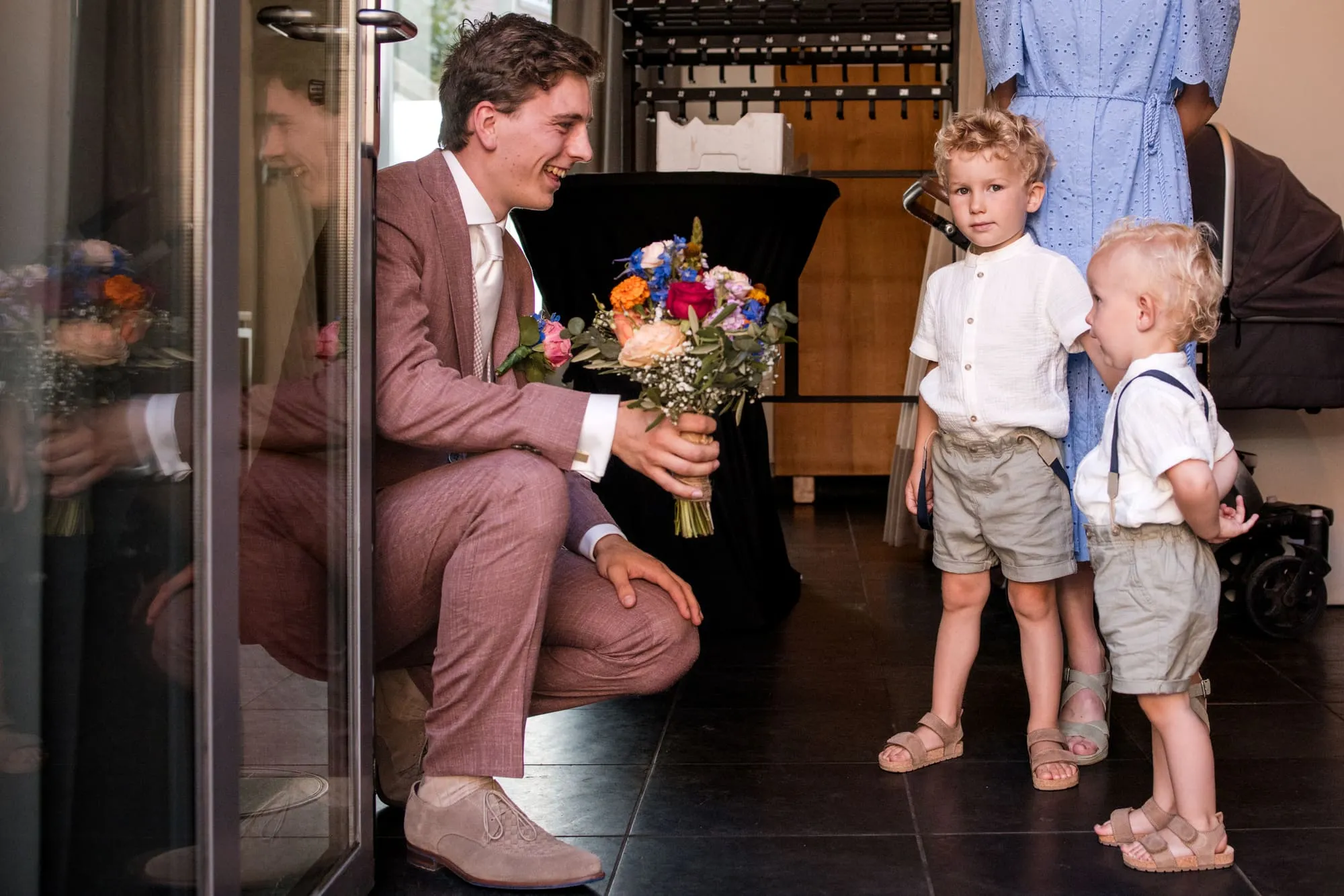 De bruidegom zit gehurkt te praten met twee jongetjes in de deuropening